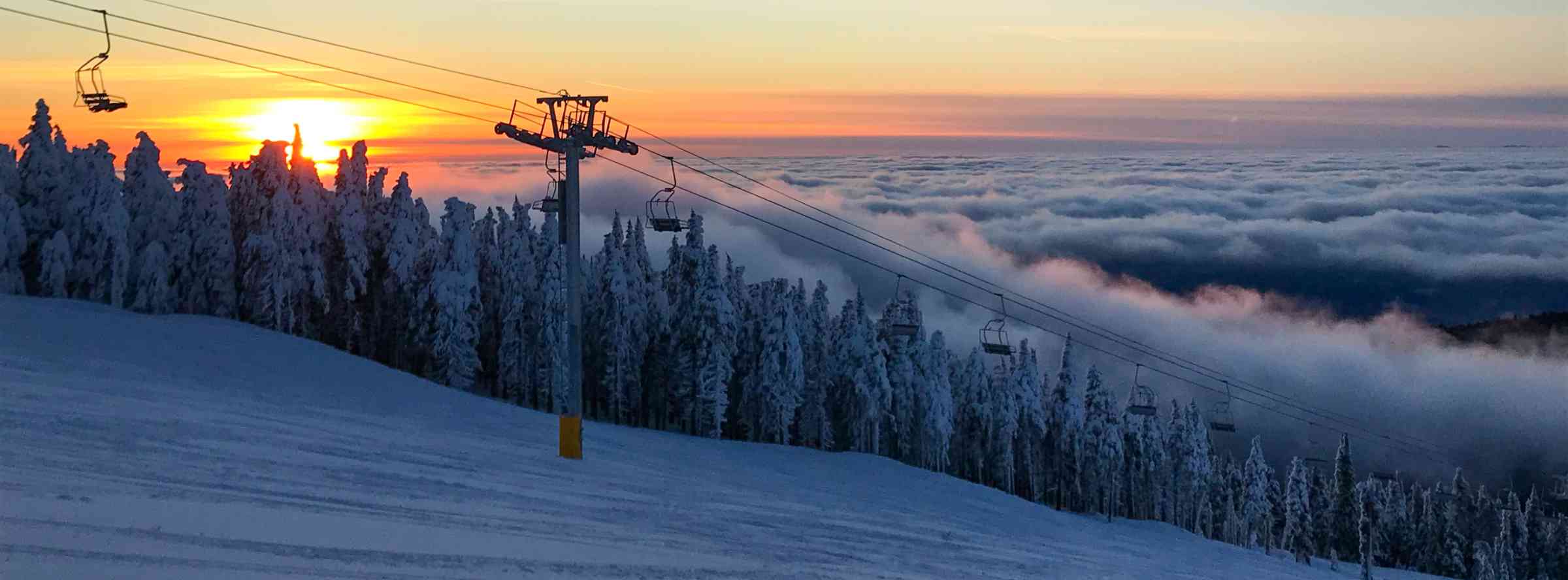 sunset over mountain chairlift and a sea of clouds